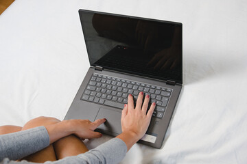 Woman's hands typing on laptop at home teleworking due to the virus pandemic. Girl in comfortable bed using laptop