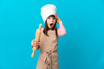 Little girl holding a rolling pin isolated on blue background with surprise expression