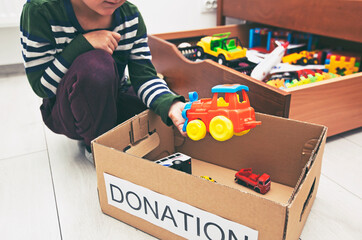 The boy is sorting his toys and puts toy car into the donation box