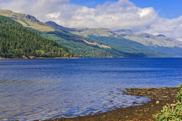 Loch Long, Argyllshire, Scotland. Beautiful Scottish scenery where fluffy white clouds cast shadows over the mountains sweeping down to the sunlit blue waters of the loch.