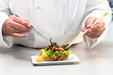 Obraz na płótnie Canvas a male chef using pliers and chopsticks to give the finishing touches to an appetizing open sandwich