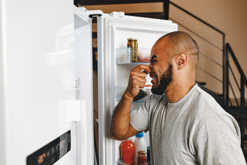 African american man closing nose because of bad smell from fridge