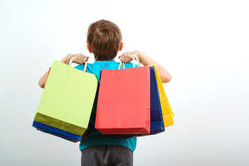 Shopping on black friday. Little boy holding shopping bags, back view. Shopper with many color paper bags.