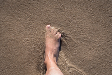 High angle shot of a person's foot on a wet sandy ground