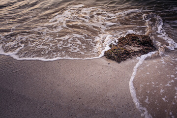 Foamy waves washing over rocky shore at sunset, close-up seascape