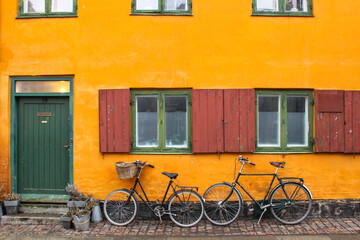 Fototapeta na wymiar Bicycles in front of an yellow orange house facade in Nyboder,historic row house district of former Naval barracks in Copenhagen, Denmark.Picturesque European city of Copenhagen.Royal Danish Navy