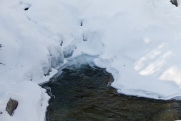 Warren falls - frozen creek under ice and snow with rocky shores. Sunny winter day