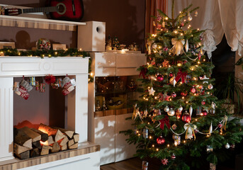 Christmas at home in the modern white living room. The Christmas tree is decorated. Artificial fireplace with socks.
