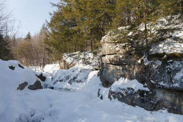 Warren falls - frozen creek under ice and snow with rocky shores. Sunny winter day