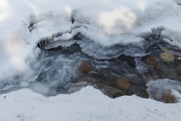 Warren falls - frozen creek under ice and snow with rocky shores. Sunny winter day