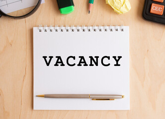 Notepad with text VACANCY on a wooden table, near calculator. Business concept.