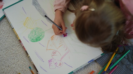 Unknown girl lying floor with colored pencils. Creative kid drawing picture home