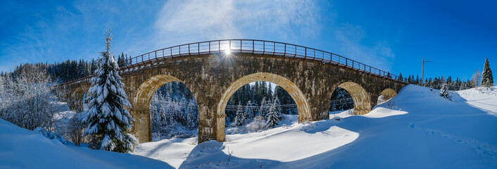 Stone viaduct (arch bridge) on railway through mountain snowy fir forest. Snow drifts  on wayside...