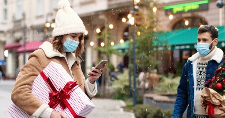 Close up portrait of Caucasian male and female lovely couple in masks having fun and fooling around on street in decorated city. Happy friends with outdoor on Christmas eve. Holidays spirit concept