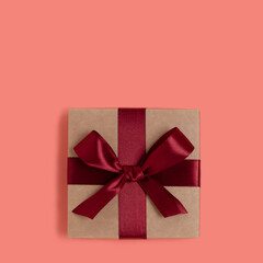 Gift box tied with red ribbon on a coral background. Festive composition.