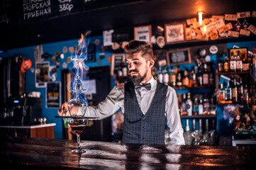 Young bartending pouring fresh alcoholic drink into the glasses on the bar