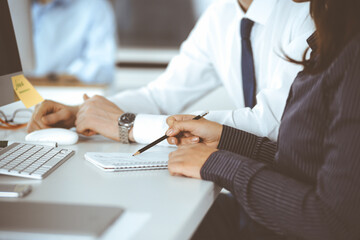 Business woman and man are discussing questions while using computer and blocknote in modern office, close-up. Teamwork in business