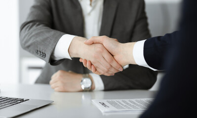 Unknown businessman shaking hands with his colleague or partner above the glass desk in modern office, close-up. Business people group at meeting