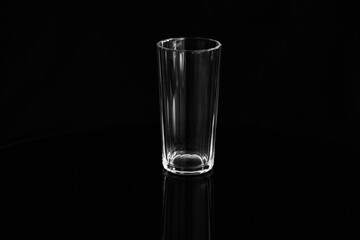Closeup of an empty glass of water on a black background. Empty glass of water on a black glossy surface.