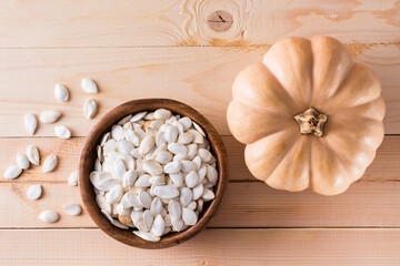 Roasted pumpkin seeds in a plate and pumpkin on a wooden table. Top view