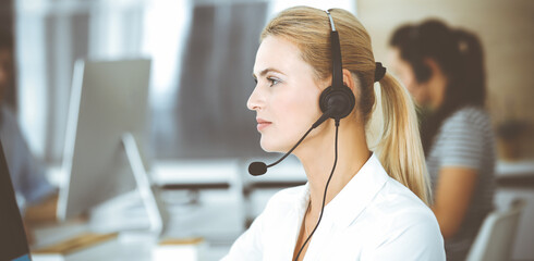 Blonde business woman using headset for communication and consulting people at customer service...