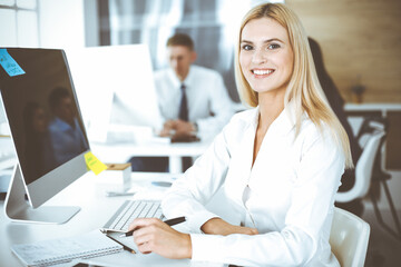 Obraz premium Business woman using computer at workplace in modern office. Secretary or female lawyer smiling and looks happy. Working for pleasure and success