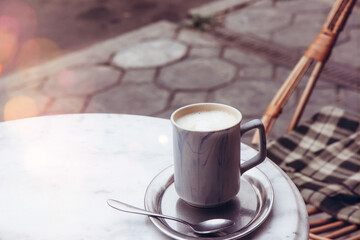 Cup of cappuccino on an iron tray on a table in a street cafe, next to the table wicker chair with a checkered plaid. Selective focus. Breakfast in a cafe. Side view