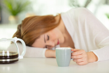 tired girl sleeping on the table holding coffee cup