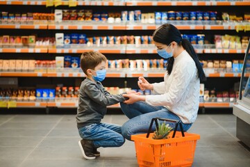 Mother applies sanitizer for cleaning son's hands in public crowded place. Shopping mall.