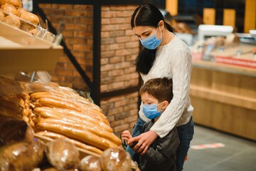 Young woman and her little son wearing protective face mask shop a food at a supermarket during the coronavirus epidemic or flu outbreak