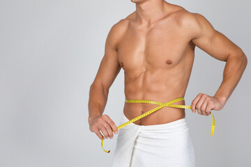 Muscular man measuring his waist with yellow tape - obrazy, fototapety, plakaty