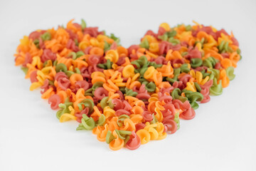 Multicolored pasta scattered on a white background in the shape of a heart. Top view. Copy, empty space for text