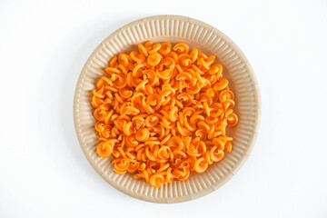 Orange pasta in a disposable paper plate on a white background. Top view. Copy, empty space for text