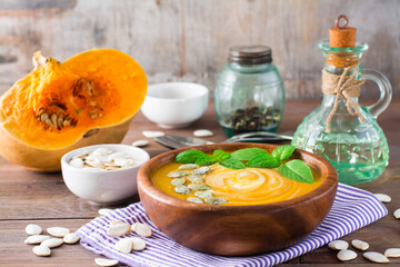 Vegetarian autumn pumpkin puree soup with seeds and cream in a wooden plate on the table. Rustic style