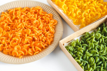 Multicolored pasta in a disposable kraft paper plates and boxes on a white background. Top view. Copy, empty space for text