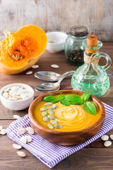 Vertical view of Vegetarian autumn pumpkin puree soup with seeds and cream in a wooden plate on the table. Rustic style