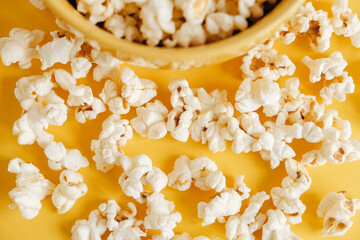 Popcorn in a yellow bowl on a yellow background. Top view. Copy, empty space for text