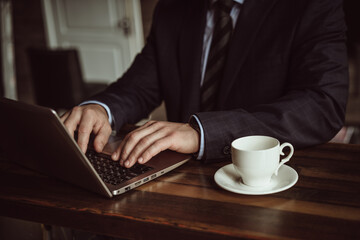 Businessman works on computer planning of business strategy. Online conference concept. Close up of male hands typing laptop keyboard sitting at office desk with cup of hot coffee on it.