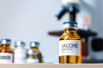 Vial of Covid-19 vaccine next to a microscope