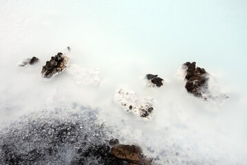 Small black rocks in milky white waters of Icelandic thermal nature baths