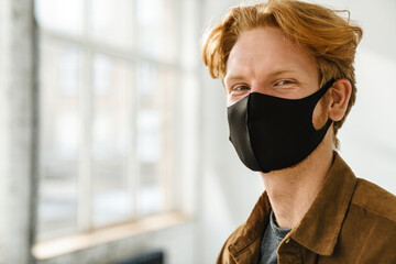 Young pleased redhead man in face mask posing and looking at camera