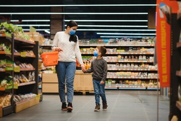 Young woman and her little son wearing protective face mask shop a food at a supermarket during the coronavirus epidemic or flu outbreak