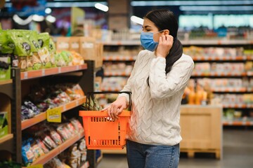 Alarmed female wears medical mask against coronavirus while grocery shopping in supermarket or store- health, safety and pandemic concept - young woman wearing protective mask and stockpiling food