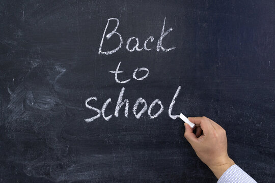 A hand writes the phrase Back to school on a chalkboard
