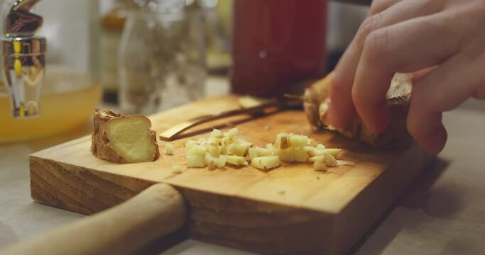 Slicing fresh ginger root on a wood cutting board. Healthy Kombucha fermented beverage homemade
