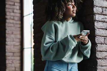 Joyful african american woman smiling and using mobile phone