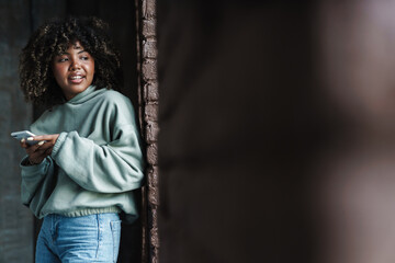 Pleased african american woman smiling and using mobile phone