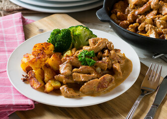 braised meat with cream sauce, vegetables and potatoes on a plate