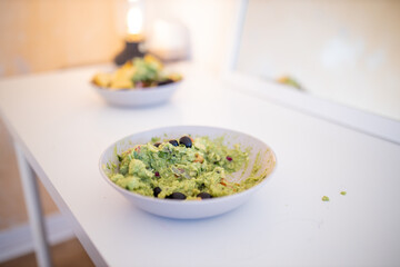 Bowl of guacamole sauce with olives on a white table