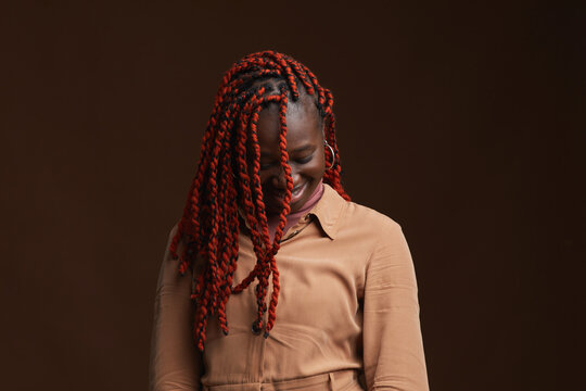 Waist Up Portrait Of Stylish African-American Woman With Braided Hair Smiling Happily While Standing Against Dark Brown Background In Studio, Copy Space